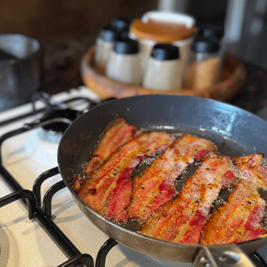 Fette di bacon affumicato a legna di faggio a rosolare in padella per la colazione dei campioni